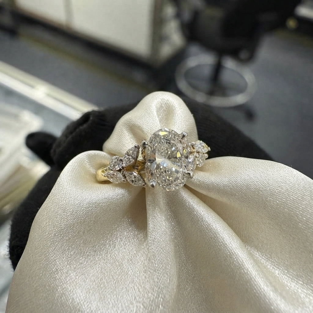 A yellow gold ring with a large round brilliant-cut center stone and smaller surrounding stones, displayed on a cream satin ribbon over a black velvet stand.